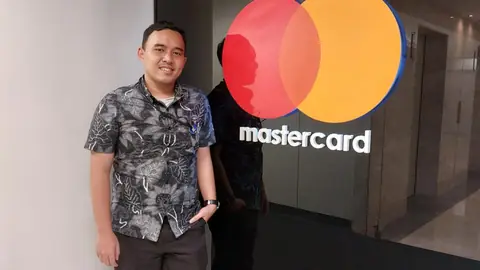 Adjie in a batik shirt next to the Mastercard logo