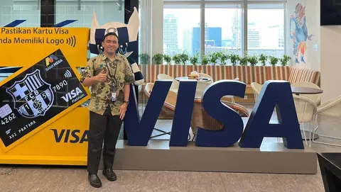 Adjie giving a thumbs up beside a large VISA sign