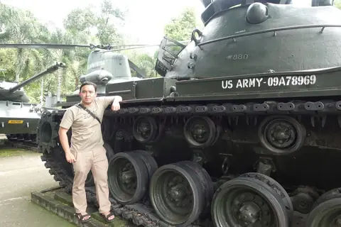 Adjie leaning on an old US Army tank, with a helicopter and another tank on display behind