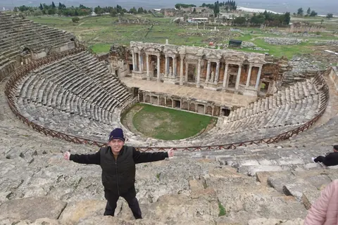Adjie with arms wide open at the top of the ancient theatre of Hierapolis, above the stage ruins
