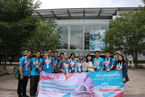 Adjie with the Scholarion Exchange group in matching shirts, holding the programme banner outside a glass building in Tokyo