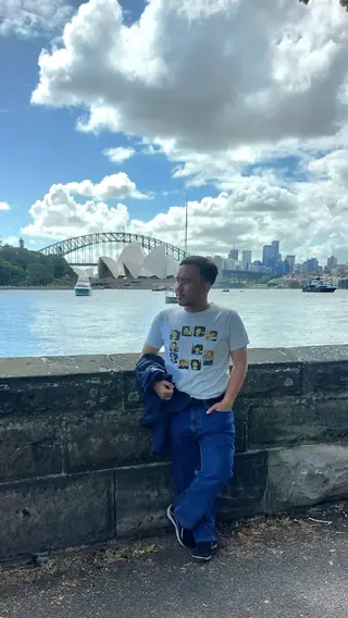 Adjie leaning on a sandstone wall across the water from the Sydney Opera House and Harbour Bridge